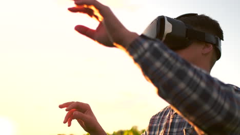 Ein-Männlicher-Bauer-Mit-Virtual-Reality-Brille,-Kariertem-Hemd-Und-Jeans-Steuert-Bei-Sonnenuntergang-Auf-Einem-Feld-Das-Maisbewässerungssystem.-Moderner-Landwirt,-Neue-Technologie,-Landwirt-Der-Zukunft