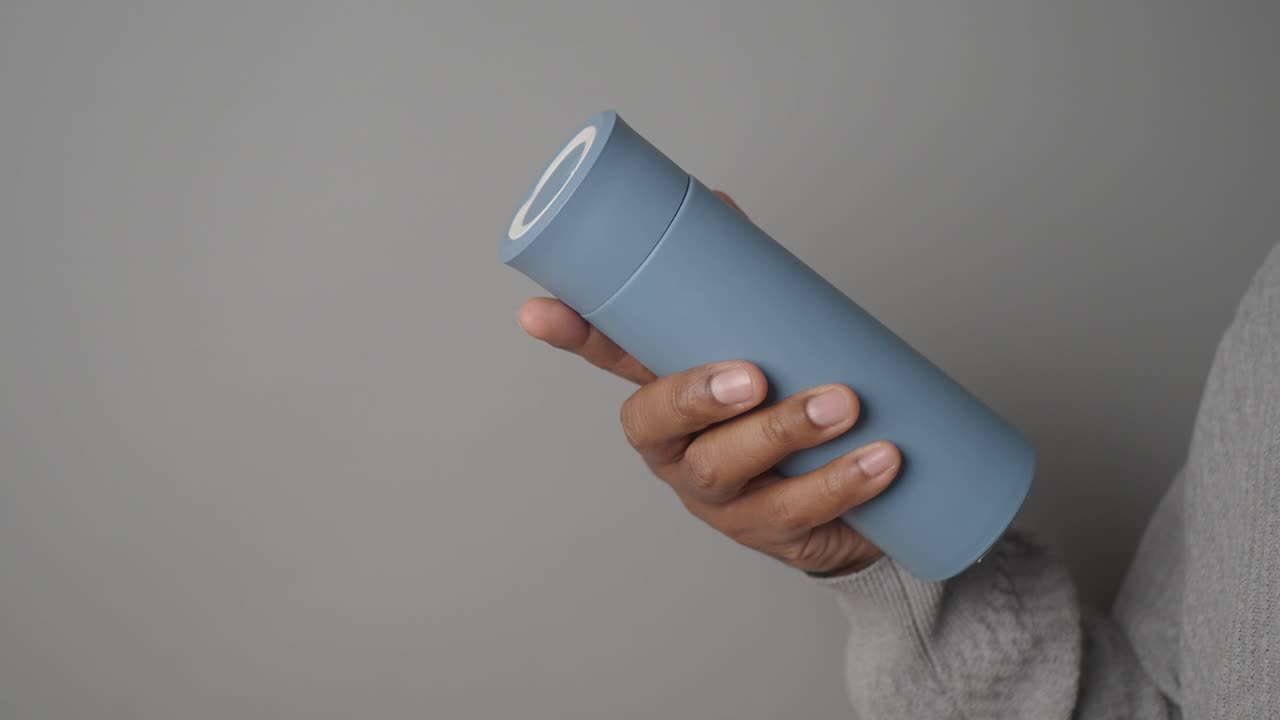 Person holding a light blue thermos