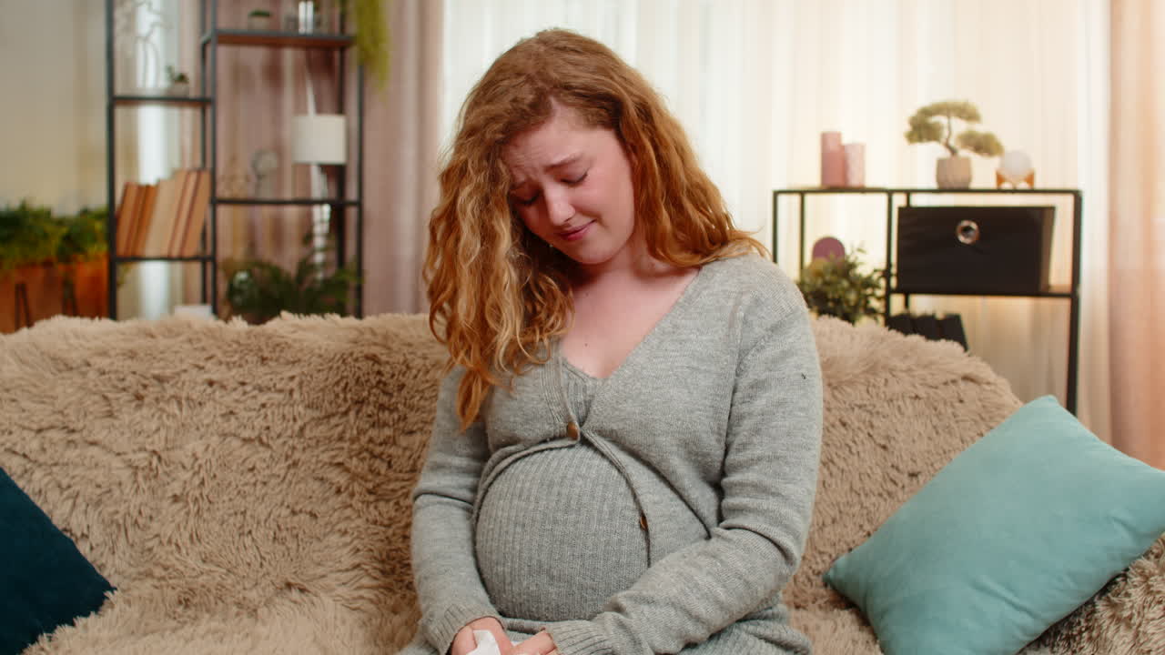 Pregnant young woman wiping tears at home holding belly emotional and sensitive moment of pregnancy