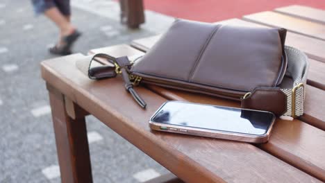 brown shoulder bag and smartphone on wooden bench