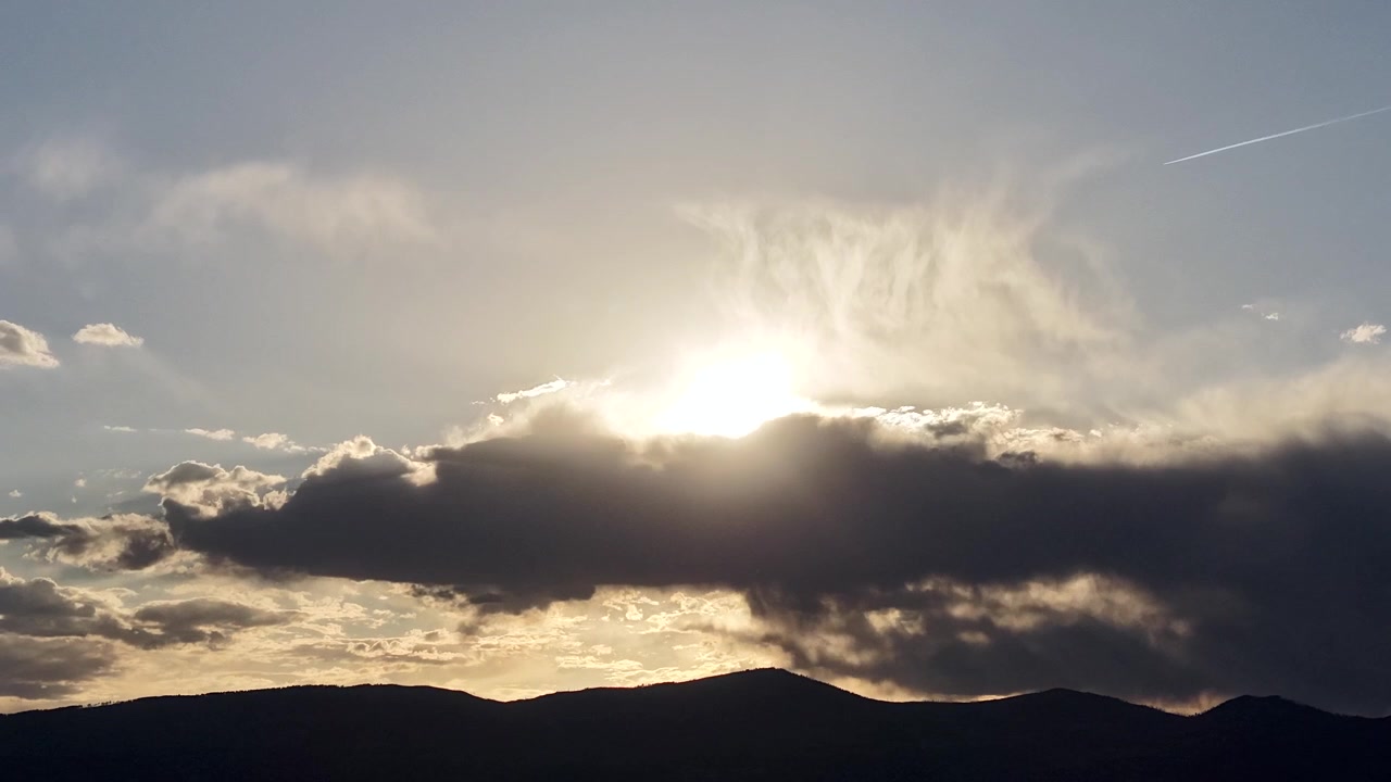 A moody atmospheric timelapse capturing the sun fading behind a thick bank of dark clouds. Glittering light rain falls across the frame, creating a beautifully textured weather transition.