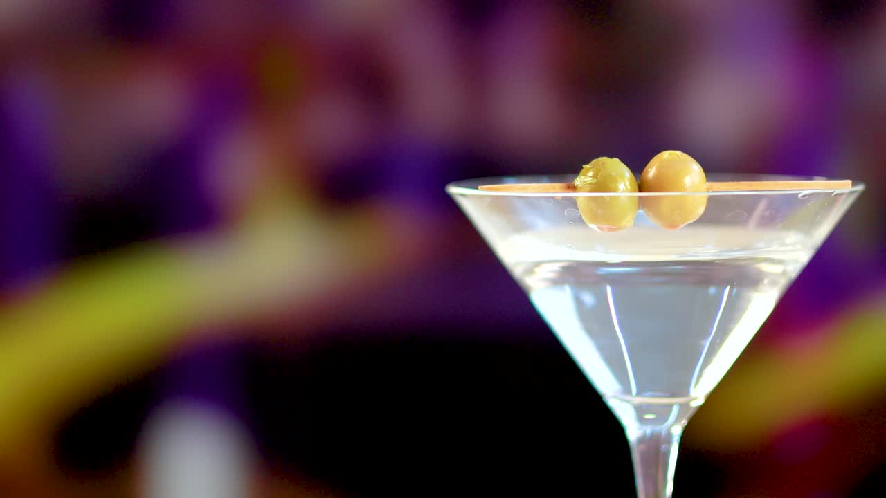 una copa de martini con aceitunas contra un fondo colorido y borroso. la iluminación brillante mejora la claridad y la elegancia de la bebida