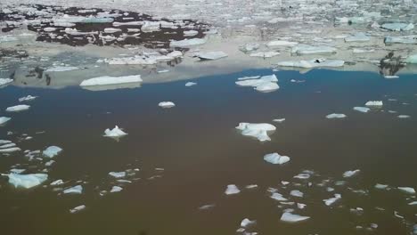 Lenta-Inclinación-Aérea-Hacia-Arriba-A-Través-De-La-Enorme-Laguna-Glaciar-Llena-De-Icebergs-En-Fjallsarlon-Islandia-Sugiere-Calentamiento-Global-Y-Cambio-Climático