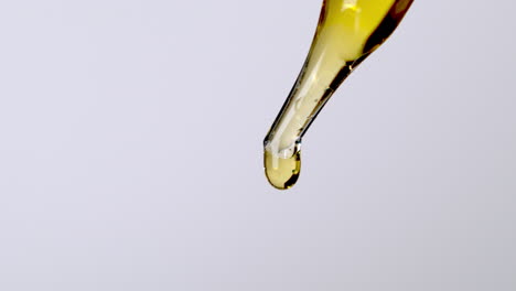 golden oil serum dripping from pipette dropper in white background