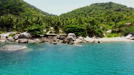 A quick zipline aerial drone shot towards the the beachfront of Ao Hin Wong and slightly panning towards the right showing some tourist swimming in its shallow waters, in Koh Tao island in Thailand
