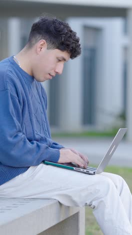 young student typing on laptop outside university. vertical