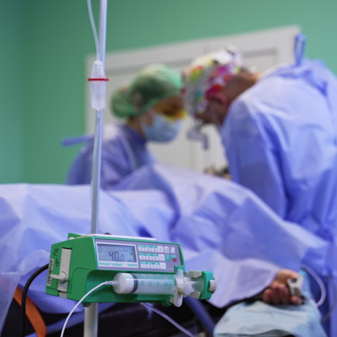 Infusion device and drop counter working in the modern surgery room. Surgical team is operating at backdrop in blur