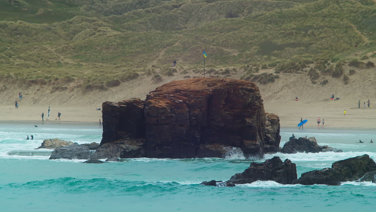 Tourists on Perranporth Beach and View of Waving Ukrainian Flag Mounted on Chapel Rock, Cornwall, England