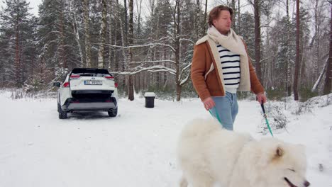 Young-caucasian-man-walking-his-Samoyed-breed-dog-though-snow-capped-forest-in-slow-motion