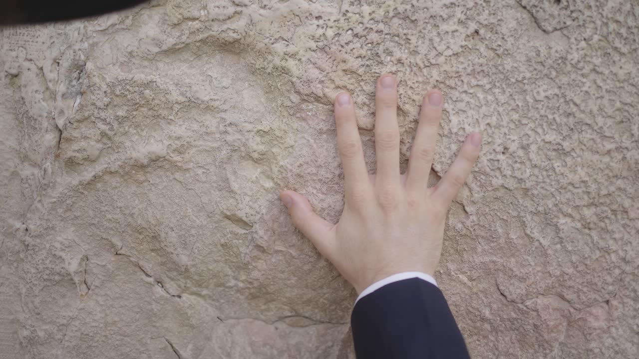 Jewish Prayer at Western Wall, Jerusalem, Israel. A religious man places his hand on the wall. The brim of his black hat is seen and it rocks in and out of frame as he recites the prayers.