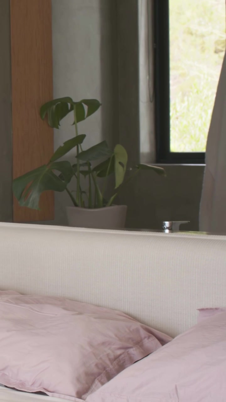 Vertical video: Smoothing man in grey T seeing hand under covers, adjusting pink pillows in bedroom