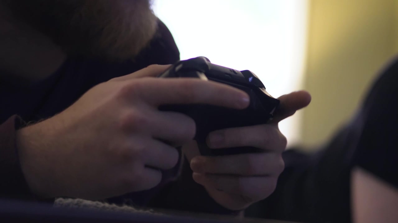 Close up shot on the hands holding a video game controller, with another man's feet kicking around in the background