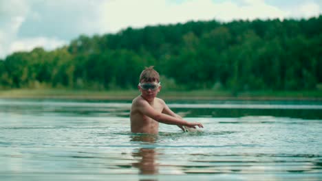 ein fröhliches kaukasisches kind mit sportausrüstung spritzt mit den händen ins wasser