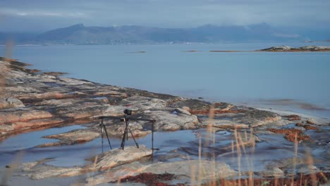 una plataforma de video profesional se encuentra en la orilla rocosa del fiordo filmando el paisaje