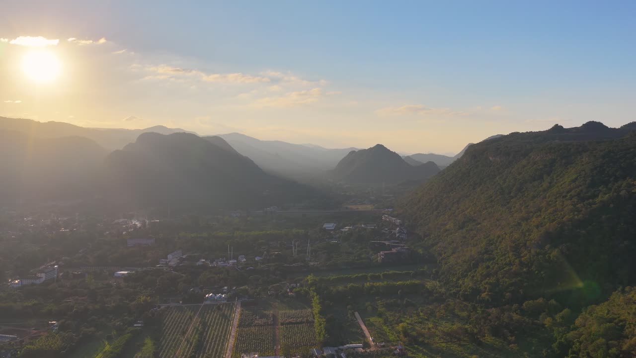 A filmagem aérea da hora dourada captura um vale montanhoso tropical e uma paisagem urbana sob a luz forte do sol