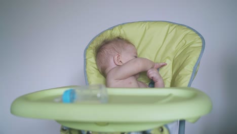 adorable bebé desnudo se sienta en una silla alta verde suave en casa