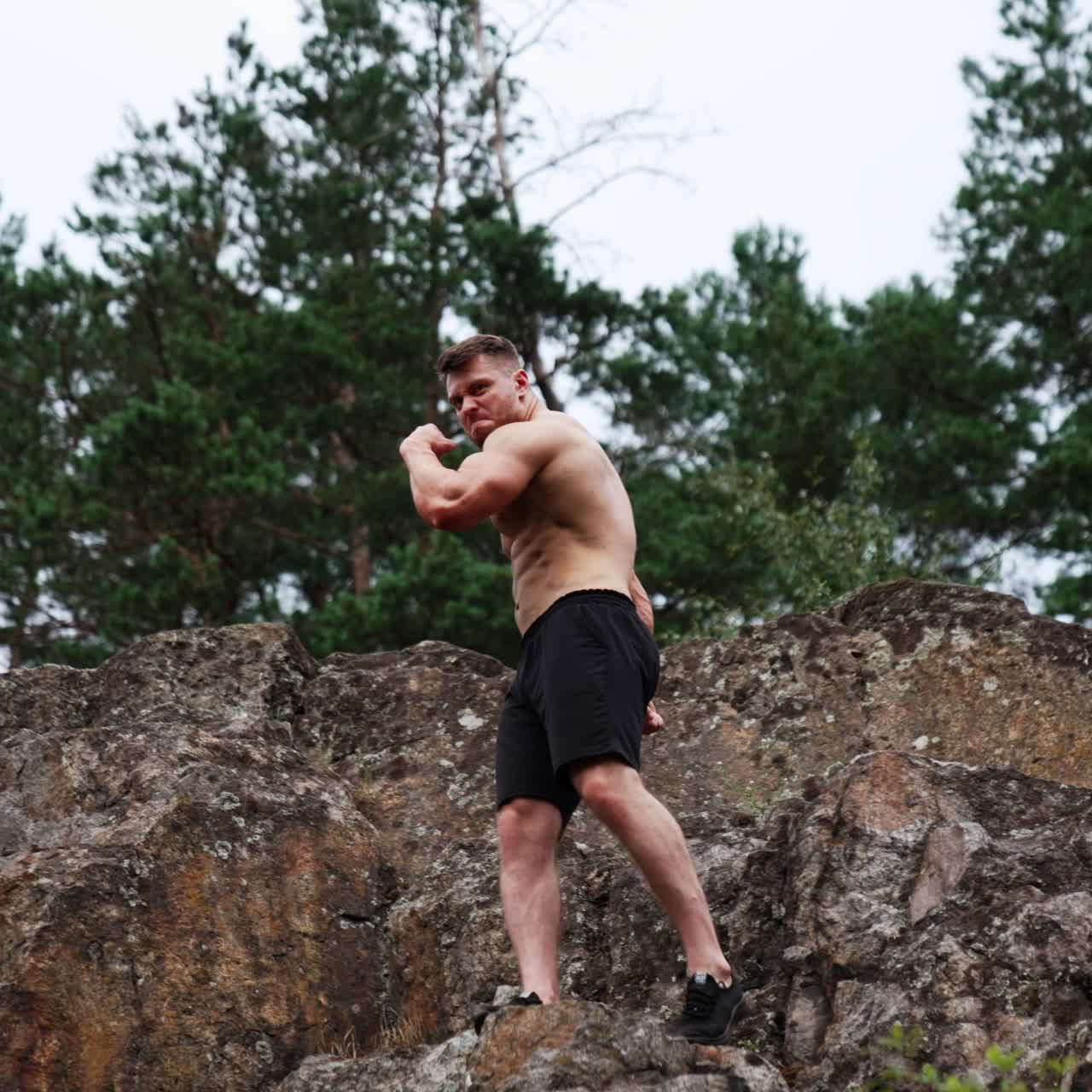 Sportsman wearing black shorts climbing by the rocks. Athlete demonstrates his muscles. Low angle view