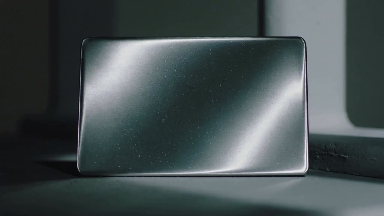 Shifting studio light moving highlights across slim rectangular device on table revealing speckles