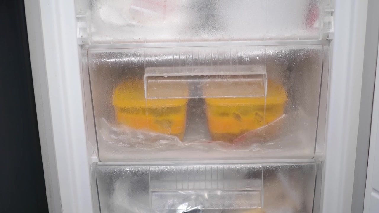 Mano che chiude un cassetto del congelatore contenente contenitori per alimenti