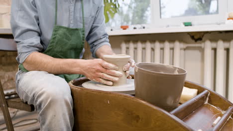 close up view of clerk in green apron modeling ceramic piece on a potter wheel in a workshop