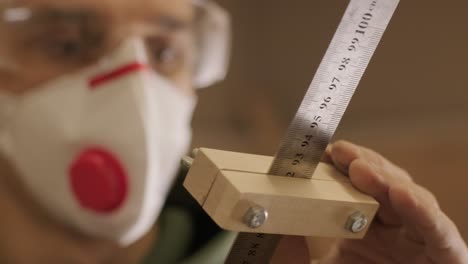 hardworking professional carpenter in mask and glasses holding a ruler