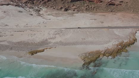 Aerial-View-Of-Car-Driving-Along-Road-Beside-Archer-Beach-In-Socotra