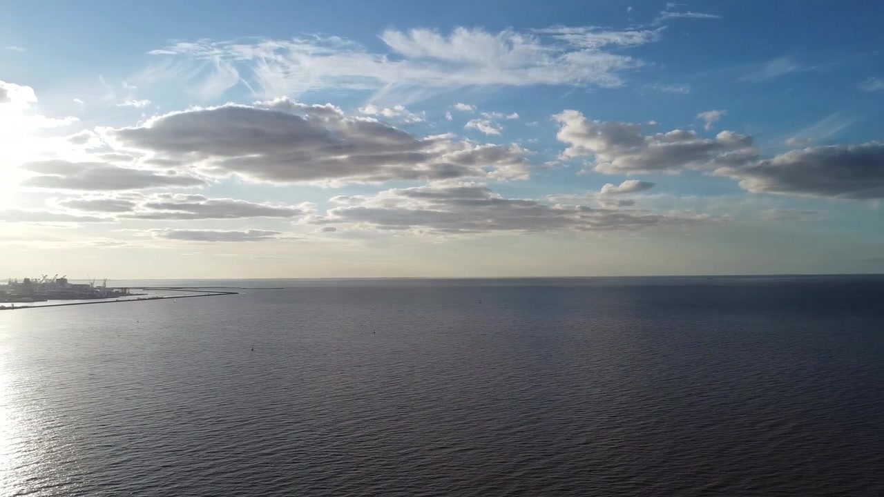 Luftoptagelse med panorering til venstre over havet med både og kyst, himmel med skyer i baggrunden