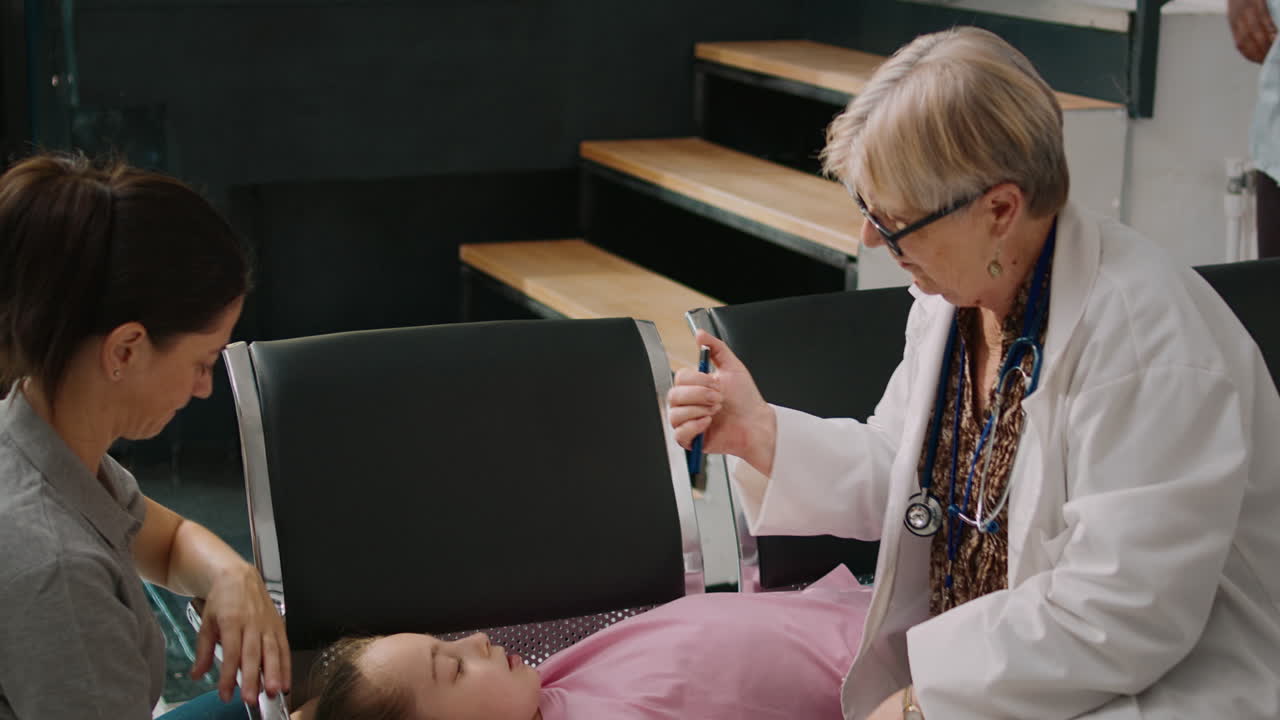 Senior medic consulting little unconscious girl with flashlight