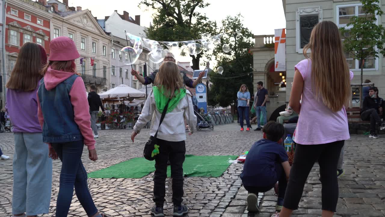 Ukraine, Lviv, Rynok Square kids playing with foam bubbles with joy. Bubble blower creates different size of foam bubbles for kids.
