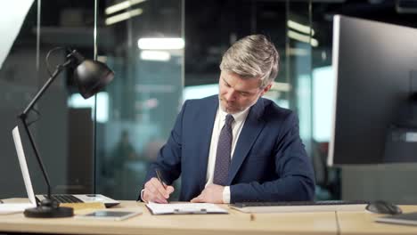 un hombre de negocios sénior firma un documento de aprobación en la oficina. un banquero o abogado exitoso un hombre de negocios leyendo y firmando un contrato de asociación comercial
