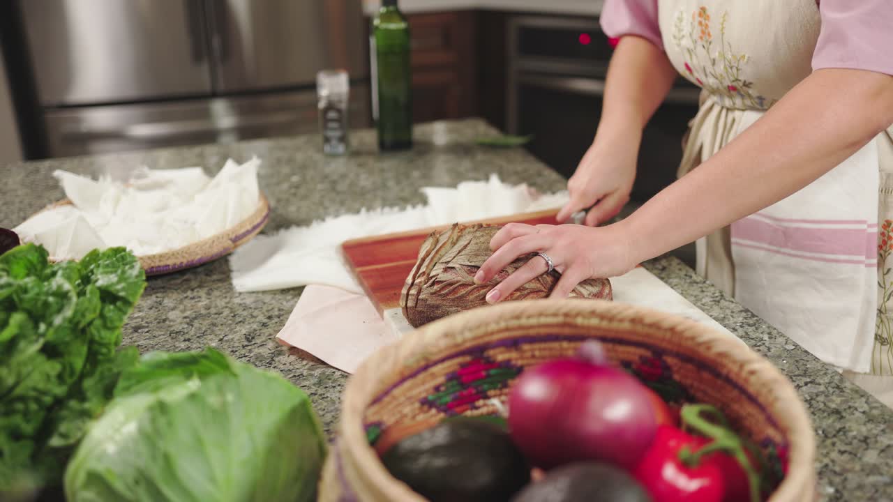 una mujer cortando un pan en un mostrador de la cocina con productos frescos cerca