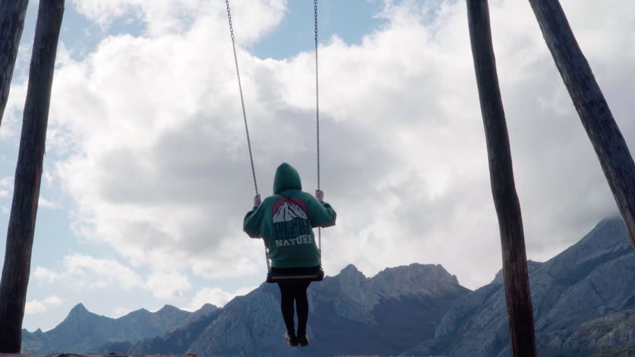 Low angle shot of a female swinging in a swing set between the high mountains