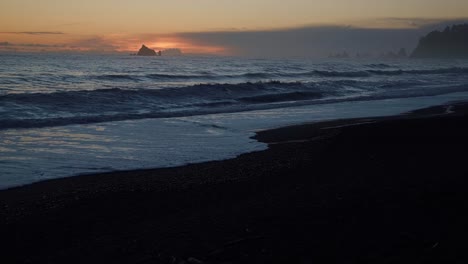 incredible stunning slow motion tilting up shot of a beautiful golden orange sunset at the famous ruby beach near forks, washington during golden hour on a warm summer day with small rocks and waves.