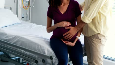 man touching pregnant womans belly in ward