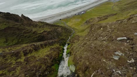 drone flying down a cliff with a waterfall at keel beach in ireland