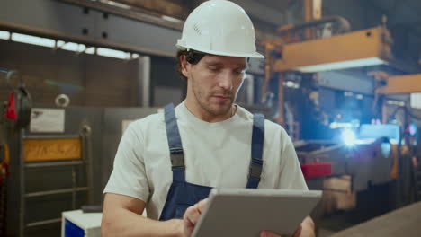 focused worker in hard hat using digital tablet in industrial factory