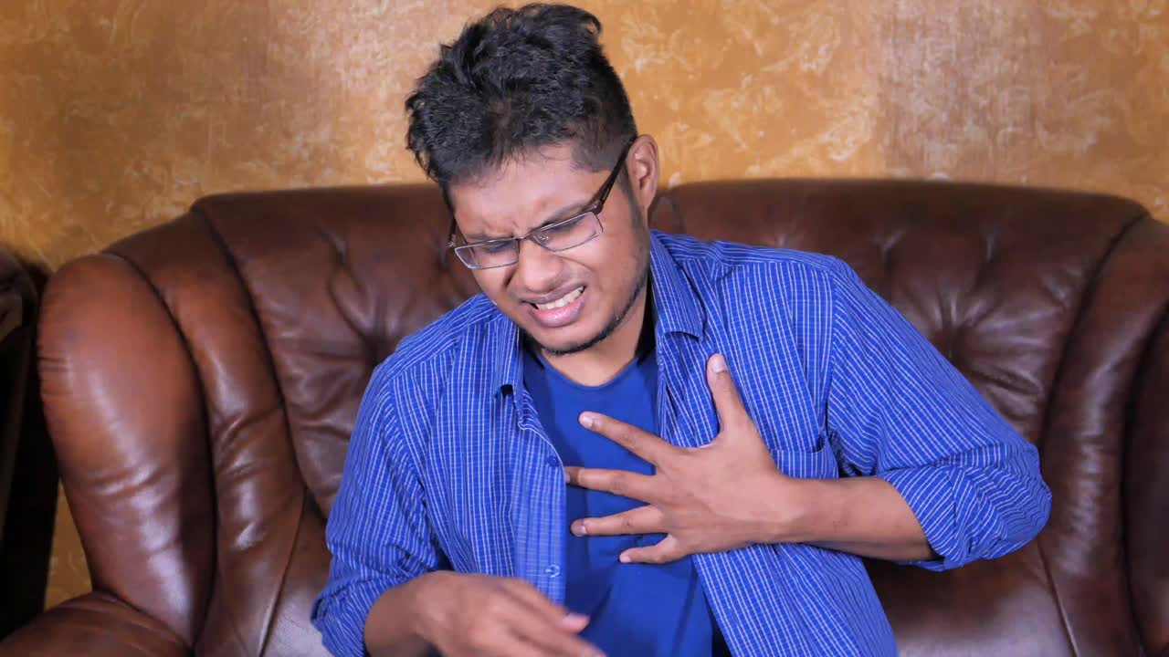 Man experiencing chest pain sitting on a brown leather couch