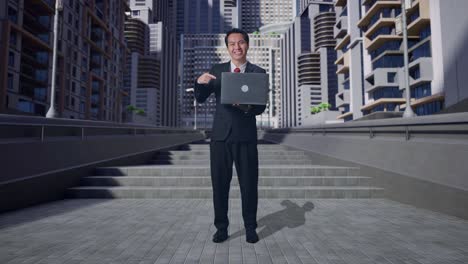 cuerpo lleno de hombre de negocios asiático sonriendo mientras usa y señala una computadora portátil en la ciudad