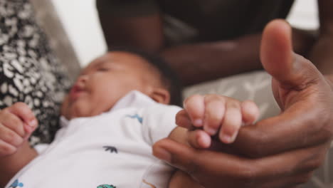 baby son gripping fathers finger as he cuddles him in nursery at home