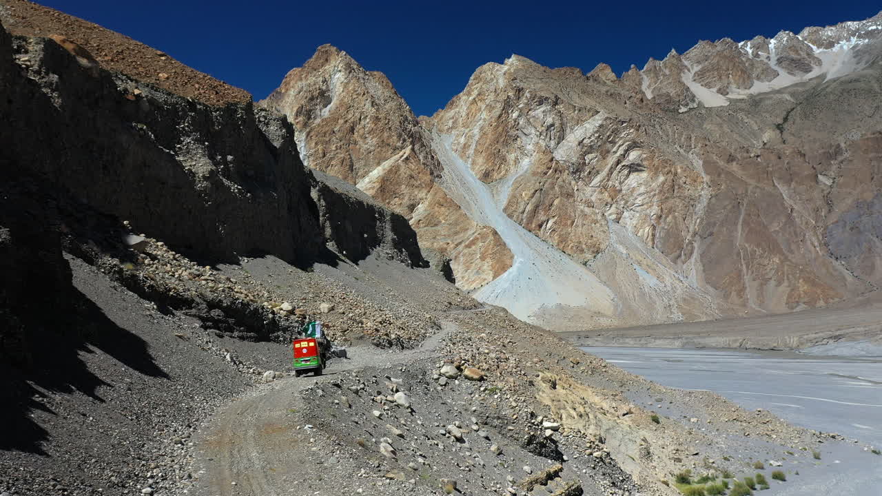 파키스탄 카라코람 고속도로의 자갈길에 있는 툭툭의 서사시 드론 샷, 멀리 있는 파수 콘, 공중 촬영