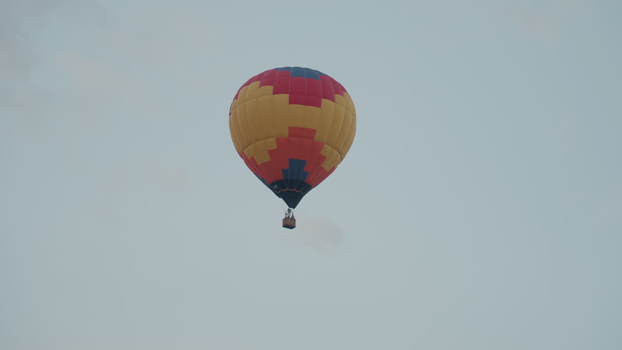 colorful hot air balloon floating high above open grass field at sunrise sky with soft clouds and pastel hues summer adventure flight scenic aerial serene calm atmosphere