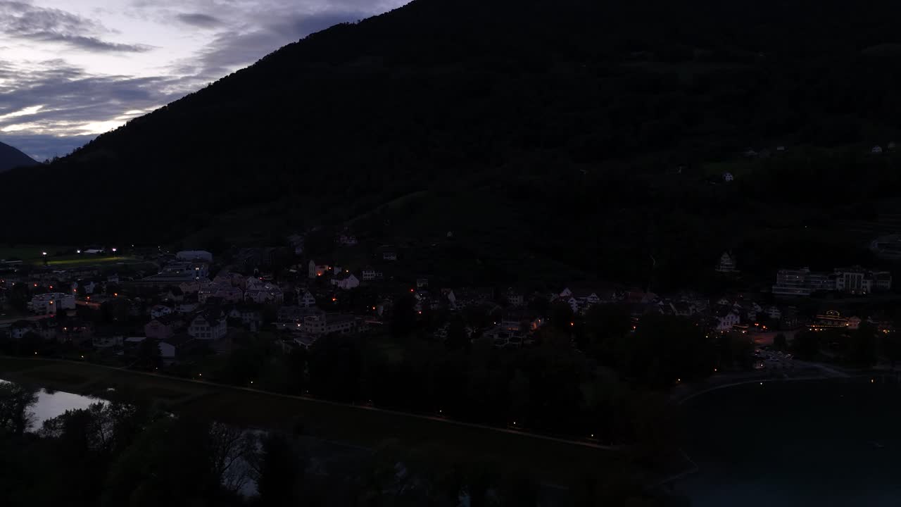 Night view of a small town nestled beside a lake and mountain