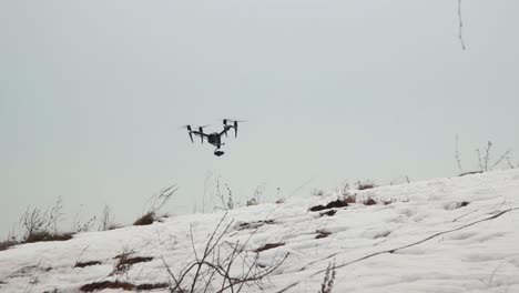 Große-Professionelle-Drohne-Dji-Inspire-2-Mit-Videokamera-Fliegt-Tief-über-Den-Schnee-Und-Weht-Dabei-Ein-Starker-Wind