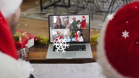 Animación-De-Nieve-Sobre-Sonriente-Padre-E-Hijo-Caucásicos-Con-Gorros-De-Papá-Noel-En-Una-Videollamada-Navideña-Con-Computadora-Portátil