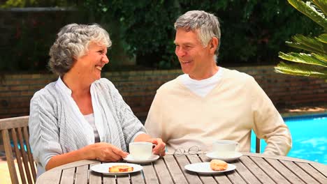 Mature-couple-having-afternoon-tea-by-a-swimming-pool