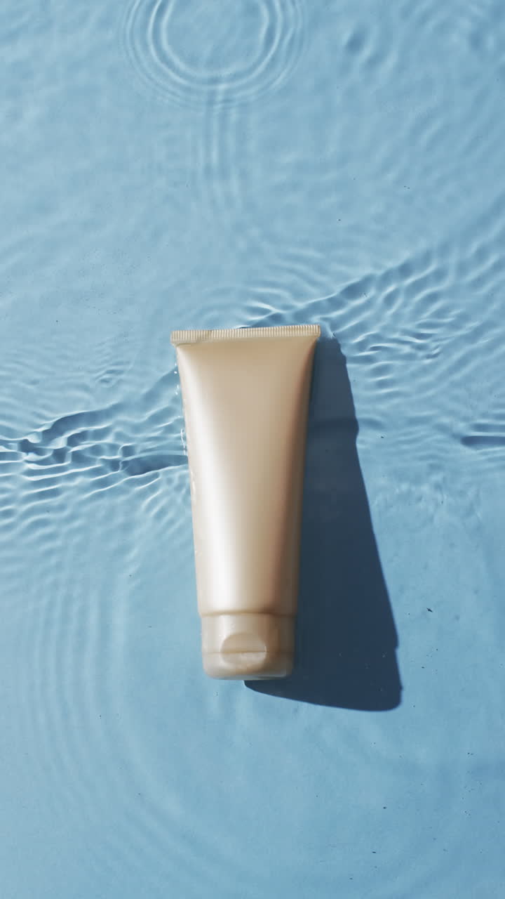 Vertical video of beauty product tube in water with copy space on blue background