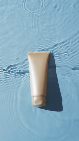 vertical video of beauty product tube in water with copy space on blue background