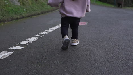 vista trasera en cámara lenta de un niño pequeño corriendo por un sendero asfaltado en el parque