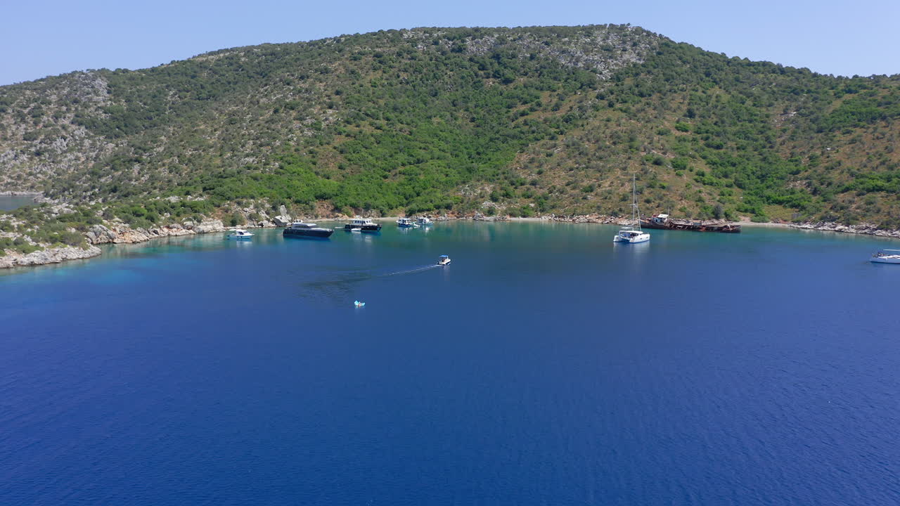 Aerial: Small boat with tourists approaches Peristera island shipwreck beach in Sporades, Greece