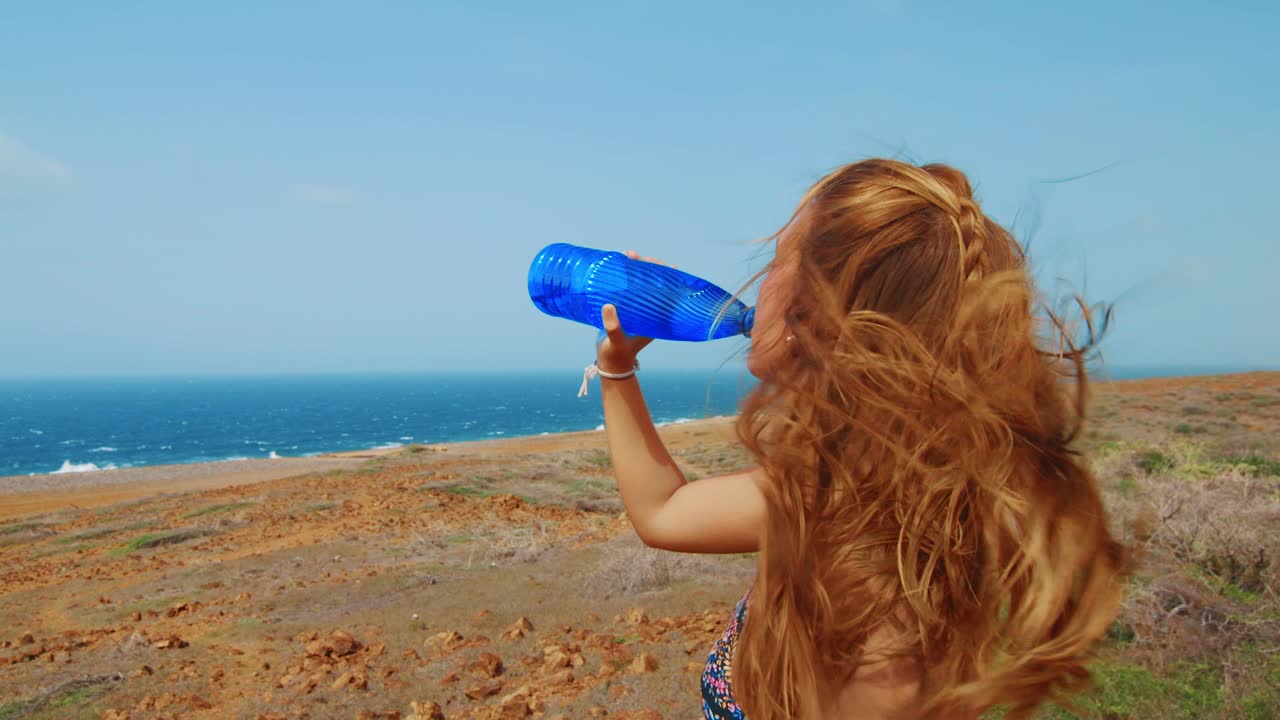 바람 부는 머리와 함께 바다로 푸른 물병에서 마시는 아름다운 여자